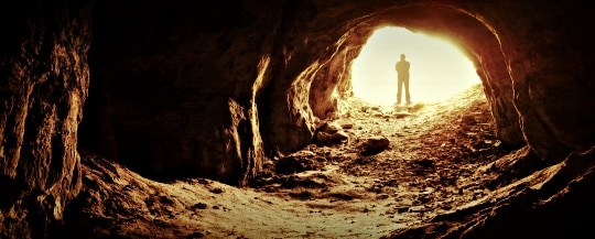 Man Standing At Cave Entrance