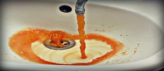 orange colored tap water running down sink drain