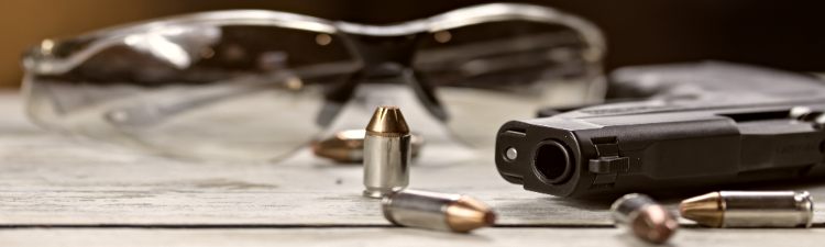 A black pistol hand gun with bullets and shooting glasses.